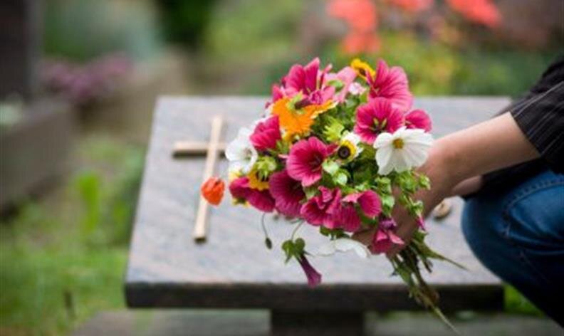A person places a bouquet of colorful flowers on a grave with a cross on the headstone.