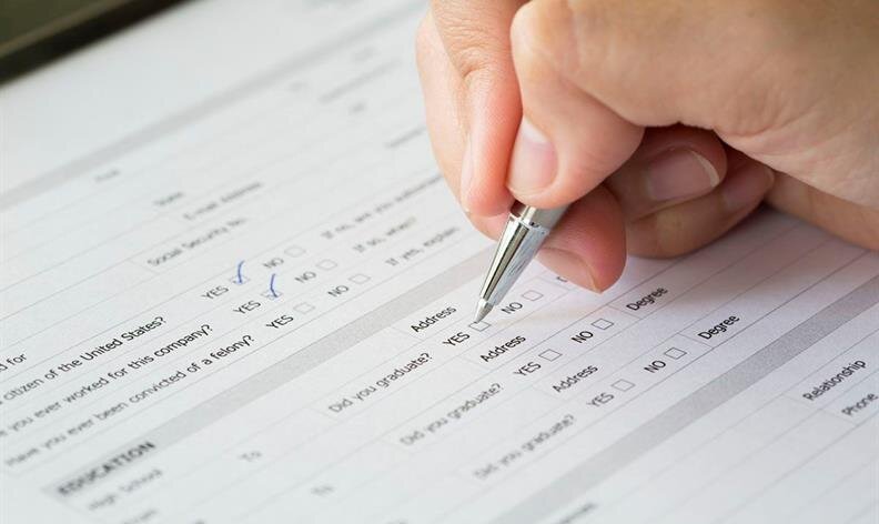 A person fills out a form with a pen, marking checkboxes labeled YES and NO on a printed questionnaire.