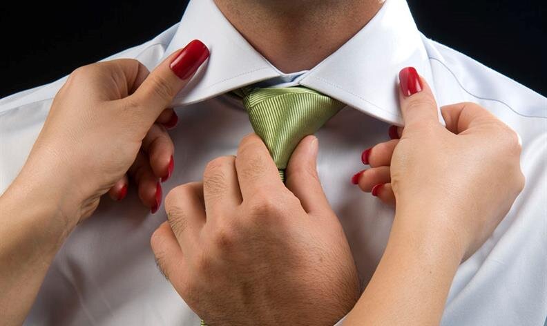 A person adjusts another person's green tie and white shirt collar; both have hands visible with red nail polish.