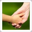 An adult hand holding a child's hand against a blurred green background.