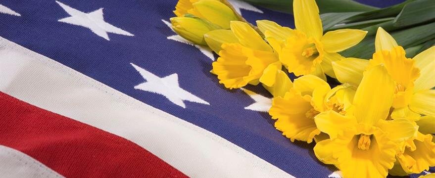 Yellow daffodils are placed on a folded American flag with visible stars and red and white stripes.